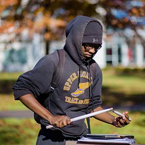 Student drumming on a notebook outside in the fall