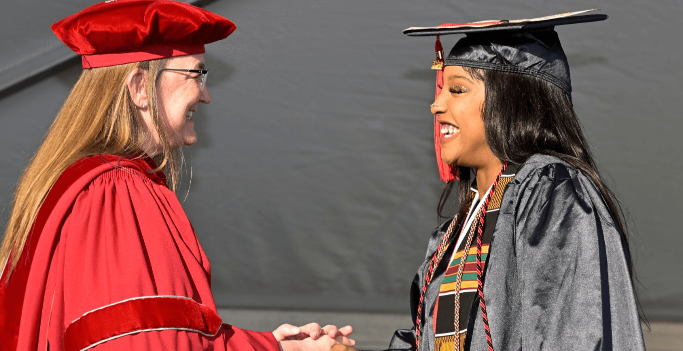 President shaking a female graduate with tassels at graduation