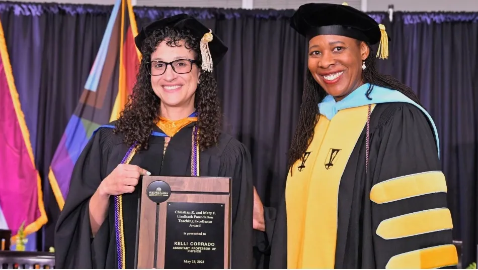 two women in graduation gowns holding a plaque