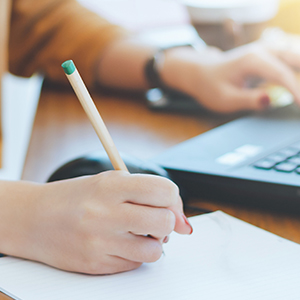 Female hands writing on paper with laptop in background