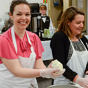 Woman in pink smiling at camera as she prepares food
