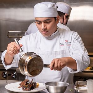 Student Chef pouring a sauce over a meal