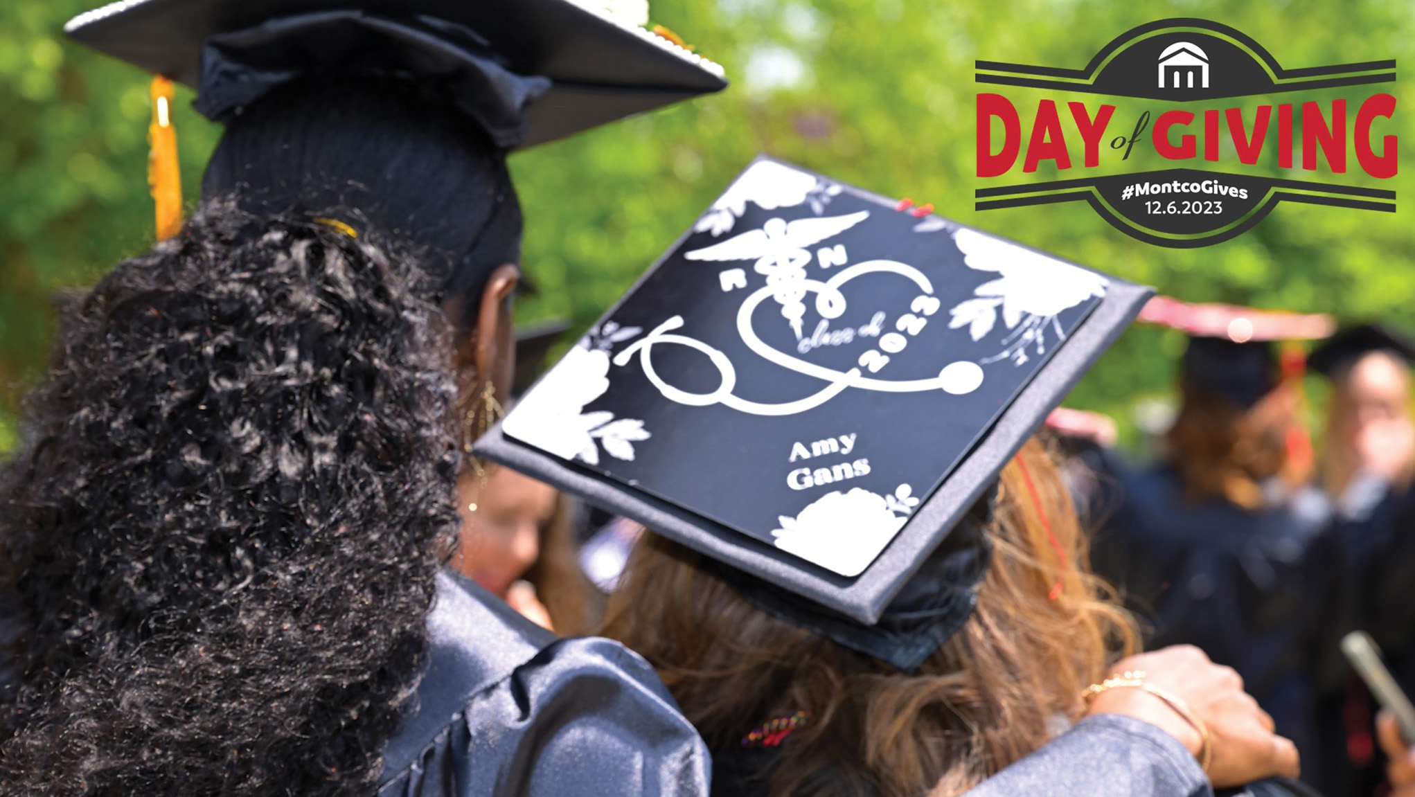 Backs of two graduates with Day of Giving logo