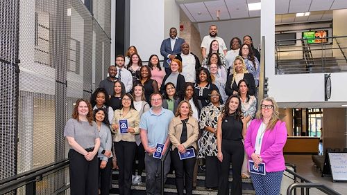Newly inducted members of Alpha Alpha Alpha National Honor Society for first generation college students stand together on a staircase in Parkhouse Hall on the Blue Bell Campus.