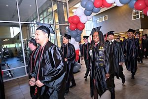 Graduates process in two lines under a balloon archway inside the Health Sciences Center