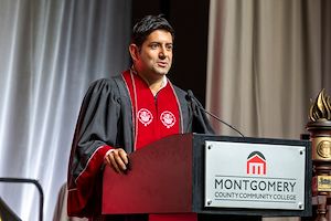 Montgomery County Commissioners Vice Chair Neil Makhija stands in red regalia giving a speech at Commencement
