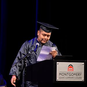 José Castillo dressed in a black cap and gown reads from prepared marks at a lectern during the Gateway to College graduation ceremony