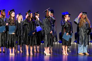 Gateway to College graduates dressed in black caps and gowns stand on stage during graduation and move the tassel on their cap from right to left signifying completion of the program