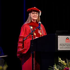 Dr. Vicki Bastecki-Perez dressed in red regalia speaks at a lectern during the Gateway to College graduation ceremony
