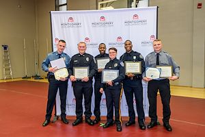 Municipal Police Academy cadets hold up their award certificates during the graduation ceremony in front of a white Montgomery County Community College backdrop