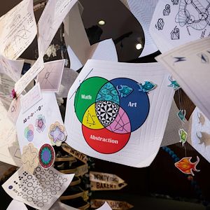 White pieces of paper with mathematics illustrations printed on them are strung together to help form the Mathemalchemy exhibit