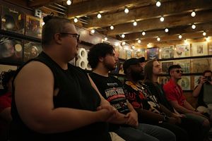 Students sit in a row in a wood panel room covered in album covers. 