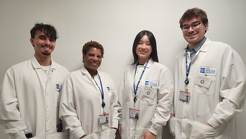 Four students dressed in white lab coats stand next to each other smiling.