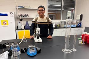 Oscar Amador standing in front of a microscope and test tubes on a laboratory table.