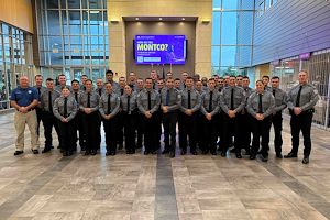 A large group of Municipal Police Academy cadets dressed in gray uniforms stand together in the lobby of the Health Sciences Center.