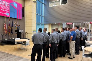 Alex Mann takes a selfie with his smartphone on a platform stage. Municipal Police Academy cadets are grouped behind him in the shot. 