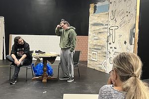 Two actors rehearse a scene from “The Aliens” with their director watching from the audience.