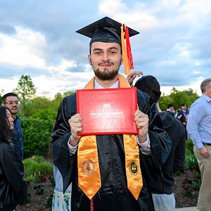 Aaron Laws dressed in a cap and gown holds his red associate's degree after Commencement