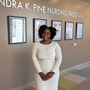 Anthonesha Anguin stands in a hallway with the words Dr. Stuart H. And Sandra K. Fine Nursing Program written on the wall behind her. 