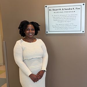 Anthonesha Anguin stands in front of a plaque that reads Dr. Stuart H. and Sandra K. Fine Nursing Program. 