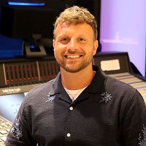 Colin Foley stands in front of a sound mixing board in the Mix Room on the Blue Bell Campus.