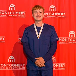 Aiden Gawel in front of a red Montco step and repeat at the nursing graduation ceremony