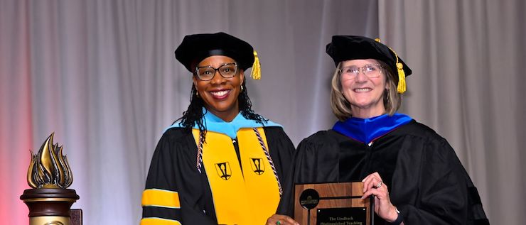 Dr. Chae Sweet and Dr. Margaret Bryans in academic regalia stand next to each other as Dr. Bryans holds a Linback Distinguished Teaching Award plaque during Commencement